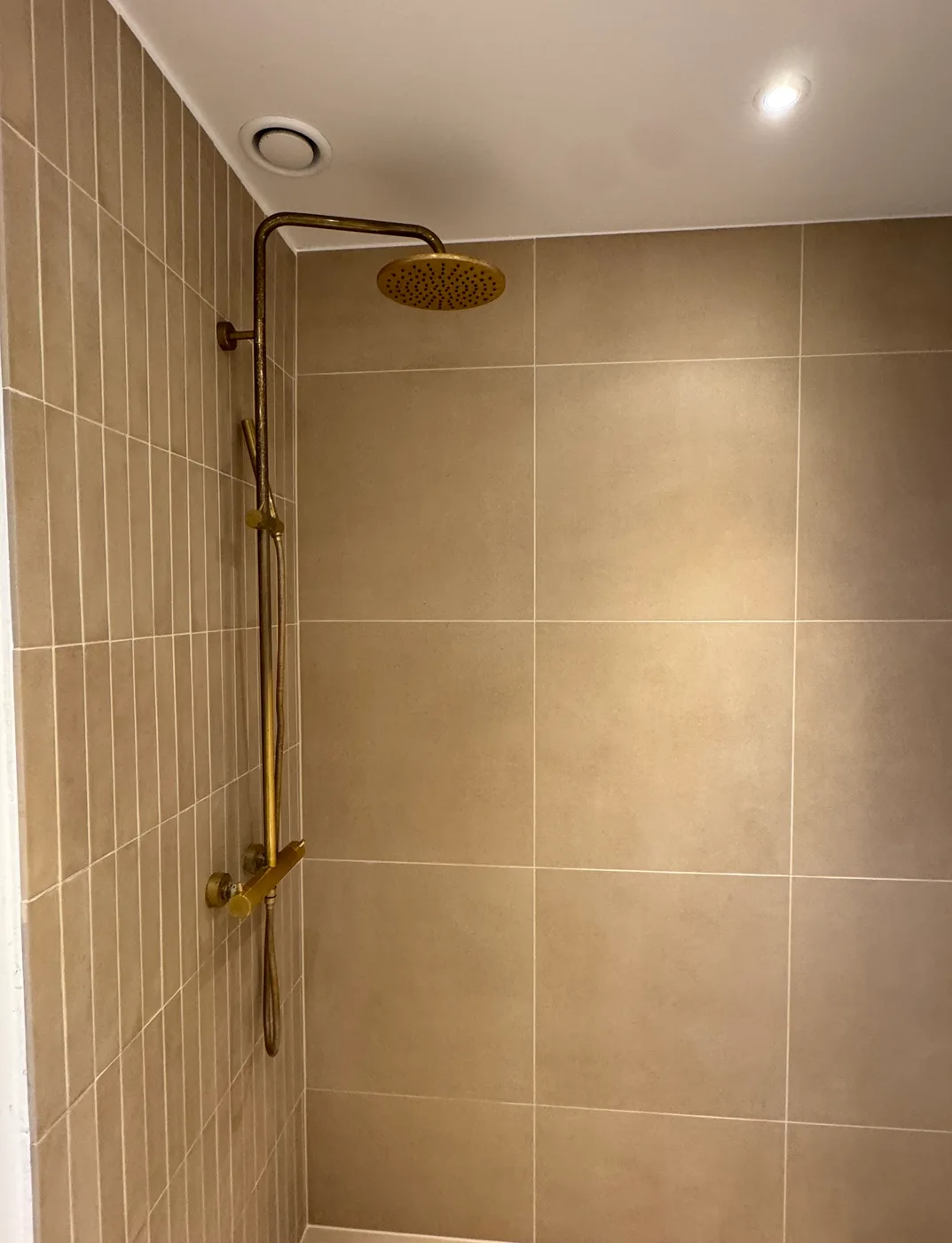 Walk-in bruser med messing regnbruser og store beige fliser — Jenrich Byg & Murer